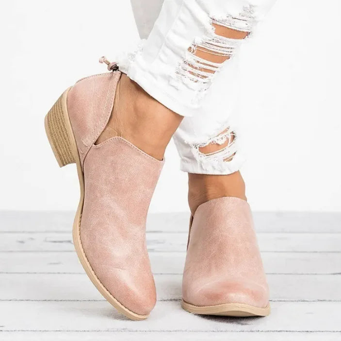 Pink slip-on shoes worn with white ripped jeans on a light wooden floor.